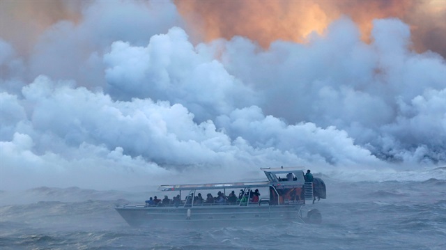 People watch from a tour boat as lava flows into the Pacific Ocean in the Kapoho area east of Pahoa during ongoing eruptions of the Kilauea Volcano in Hawaii US