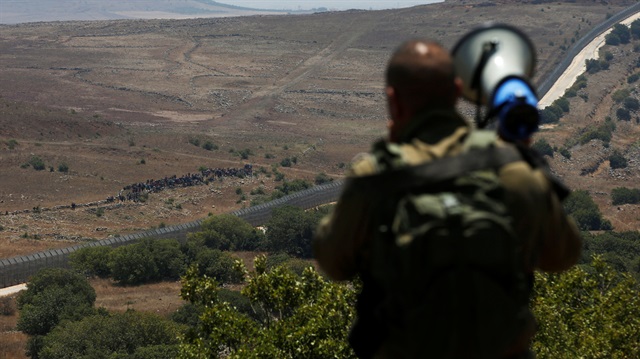 An Israeli soldier speaks over a megaphone to people which stand next to the border fence between Israel and Syria from its Syrian side as it is seen from the Israeli-occupied Golan Heights near the Israeli Syrian border July 17, 2018. 