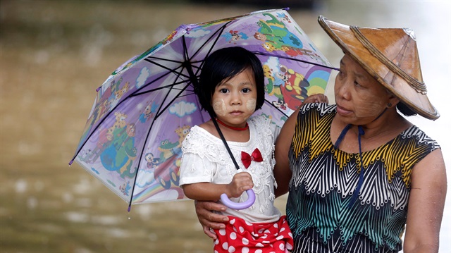 File photo: A woman carries her daughter as she walks on a flooded street in Kyaikto township, Mon state, Myanmar
