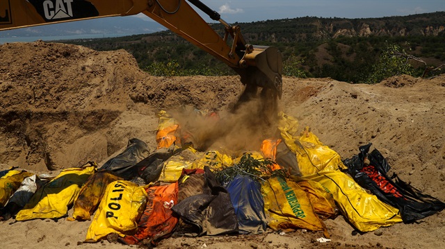 Sand is placed over dead bodies of the victims of the earthquake and tsunami during a mass burial at the Poboya Cemetery in Palu, Central Sulawesi, Indonesia, October 2, 2018. 