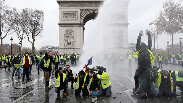 Protesters wearing yellow vests, a symbol of a French drivers' protest against higher diesel taxes, stand up in front of a police water canon at the Place de l'Etoile near the Arc de Triomphe in Paris, France